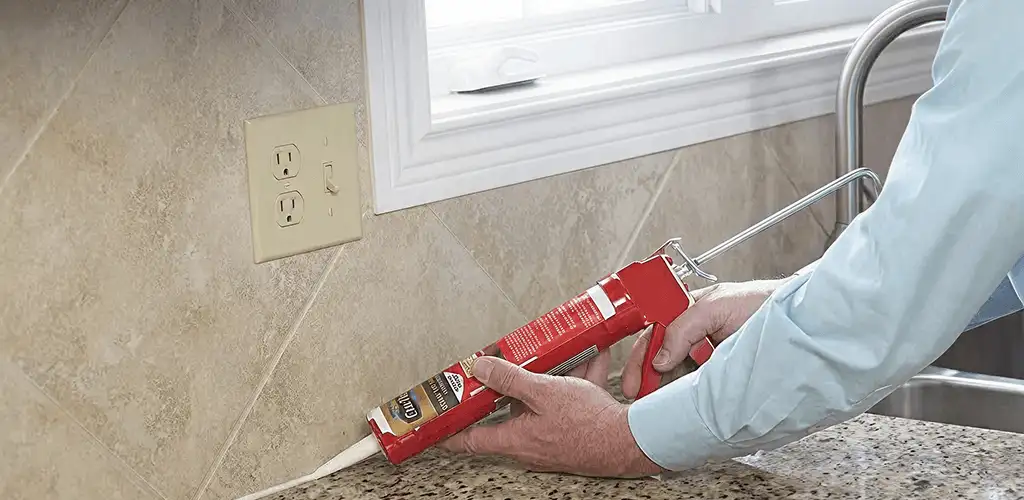 Handyman applying caulk along a kitchen backsplash and countertop seam in Philadelphia, PA
