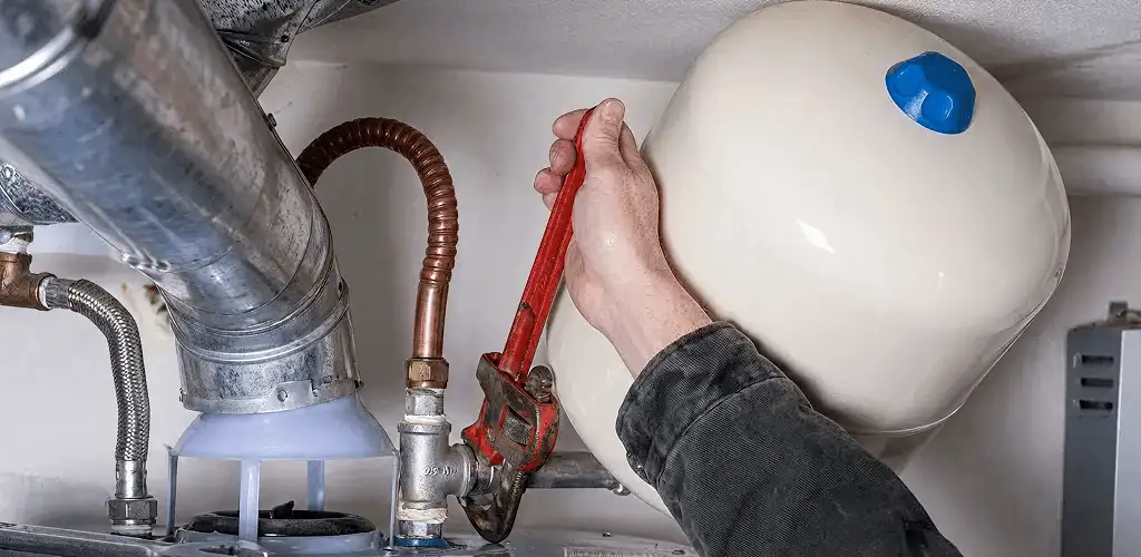 Water heater repair technician tightening plumbing connections near a tank unit in Philadelphia, PA
